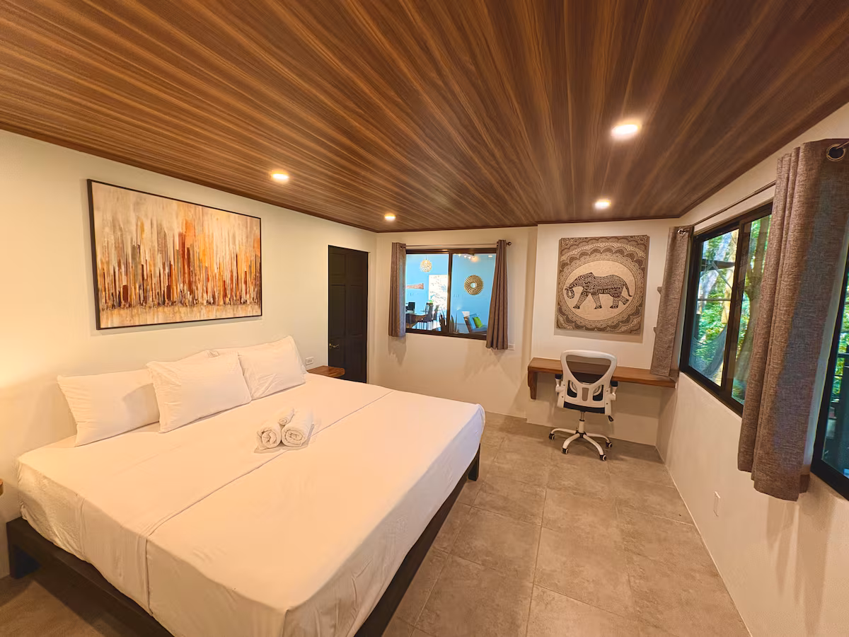 Grande chambre de la Villa 6 avec lit king size, espace bureau et vue sur la nature à Uvita