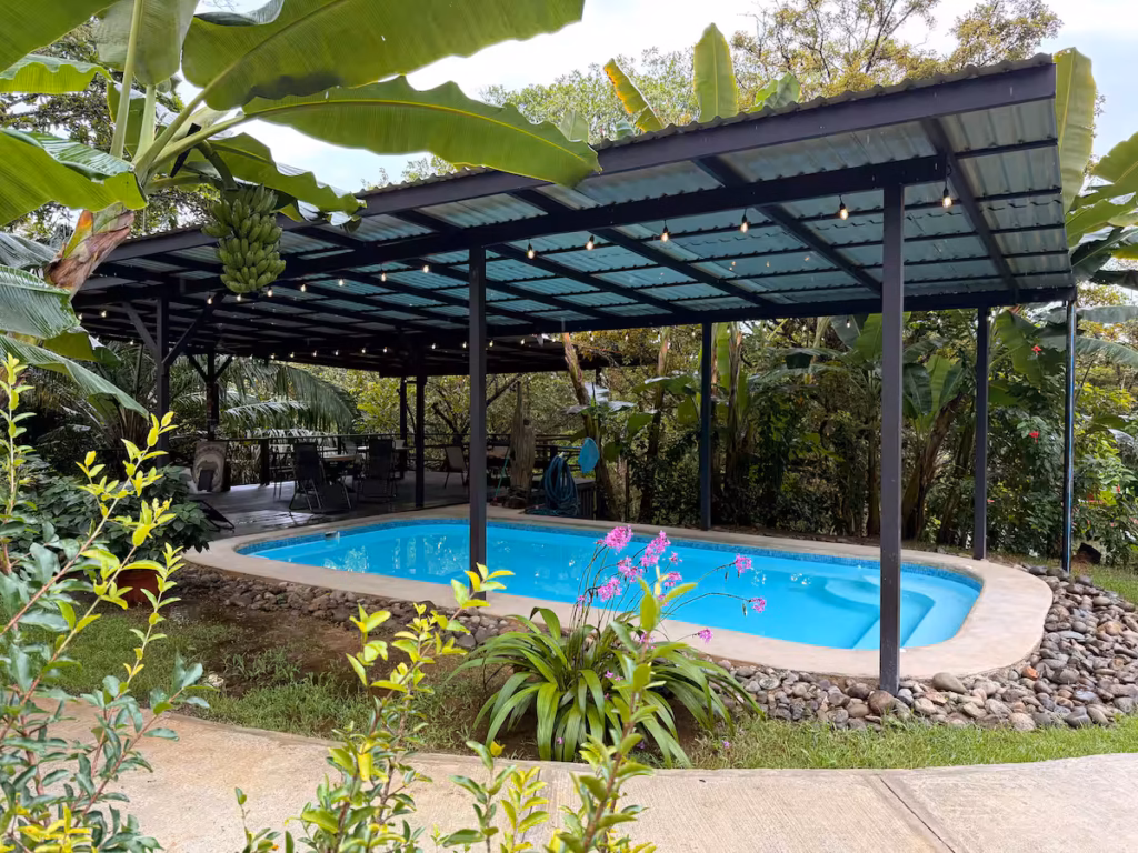 Piscine extérieure avec terrasse couverte et espace de repos entourés de jardins tropicaux.