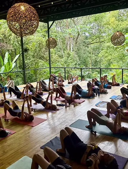 Participants à une séance de yoga sur une plateforme ouverte entourée de végétation tropicale.