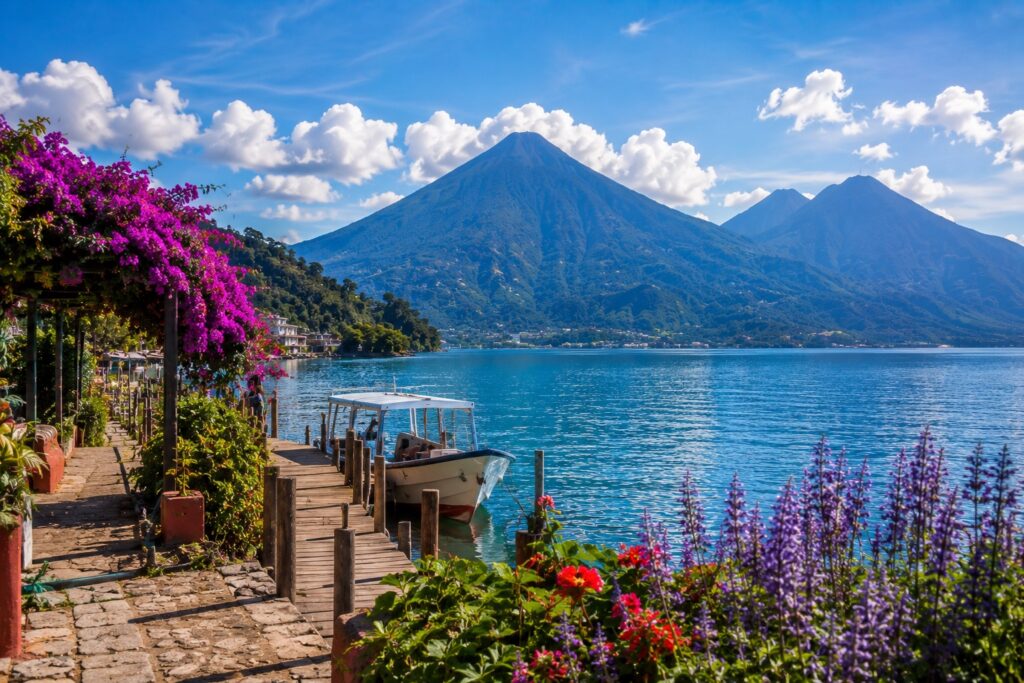 Circuit Guatemala – Vue panoramique de San Juan La Laguna sur le lac Atitlán avec un embarcadère, un bateau traditionnel et les volcans du Guatemala.